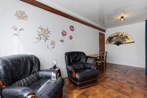 A room with two leather chairs, a wooden table, a fan, and a wall with floral decorations.