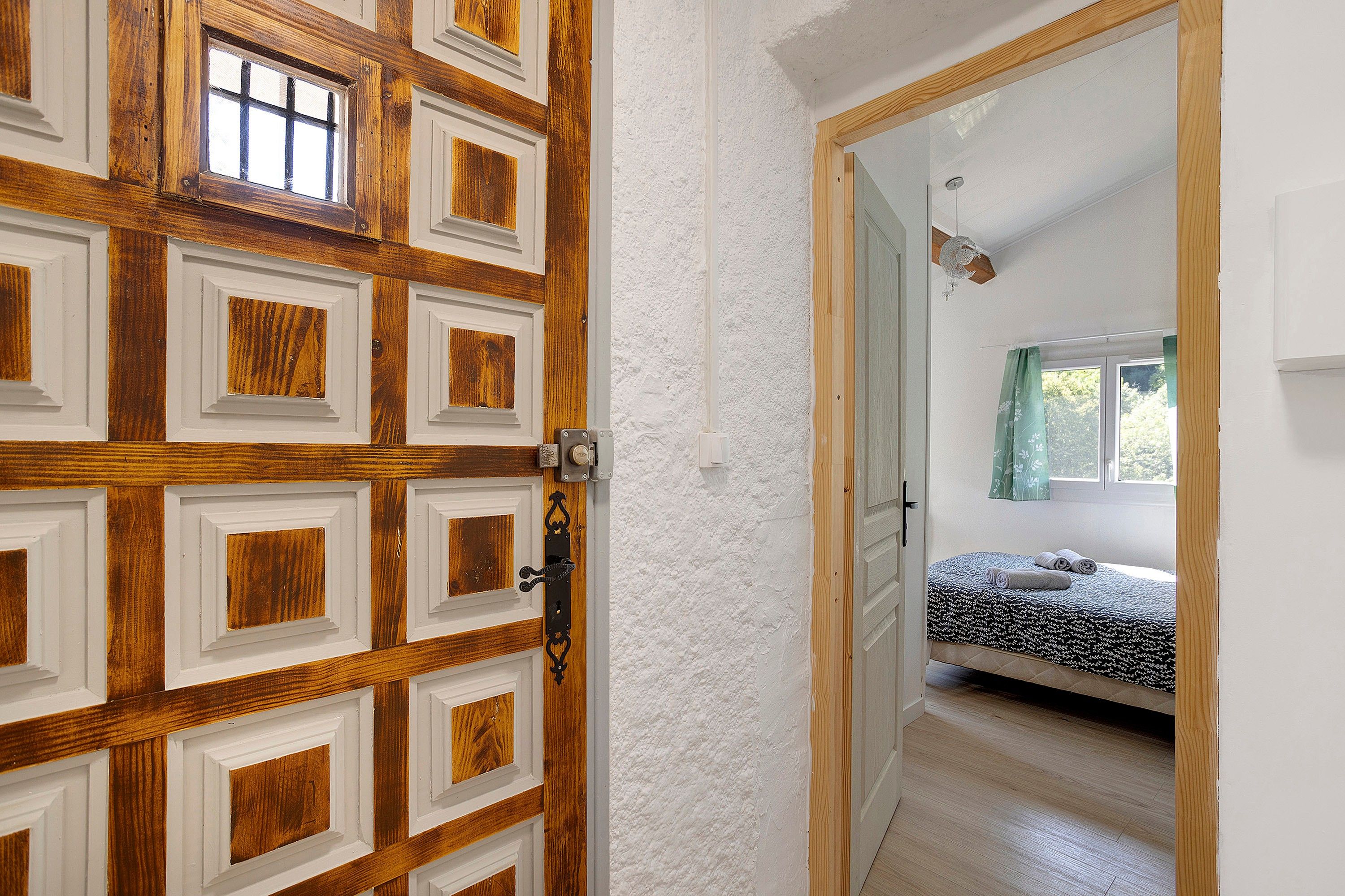 Una habitación con una cama, un ventanal con cortinas y una puerta con detalles de madera.