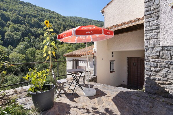 A balcony with a table and chairs, a potted plant, and a red umbrella.