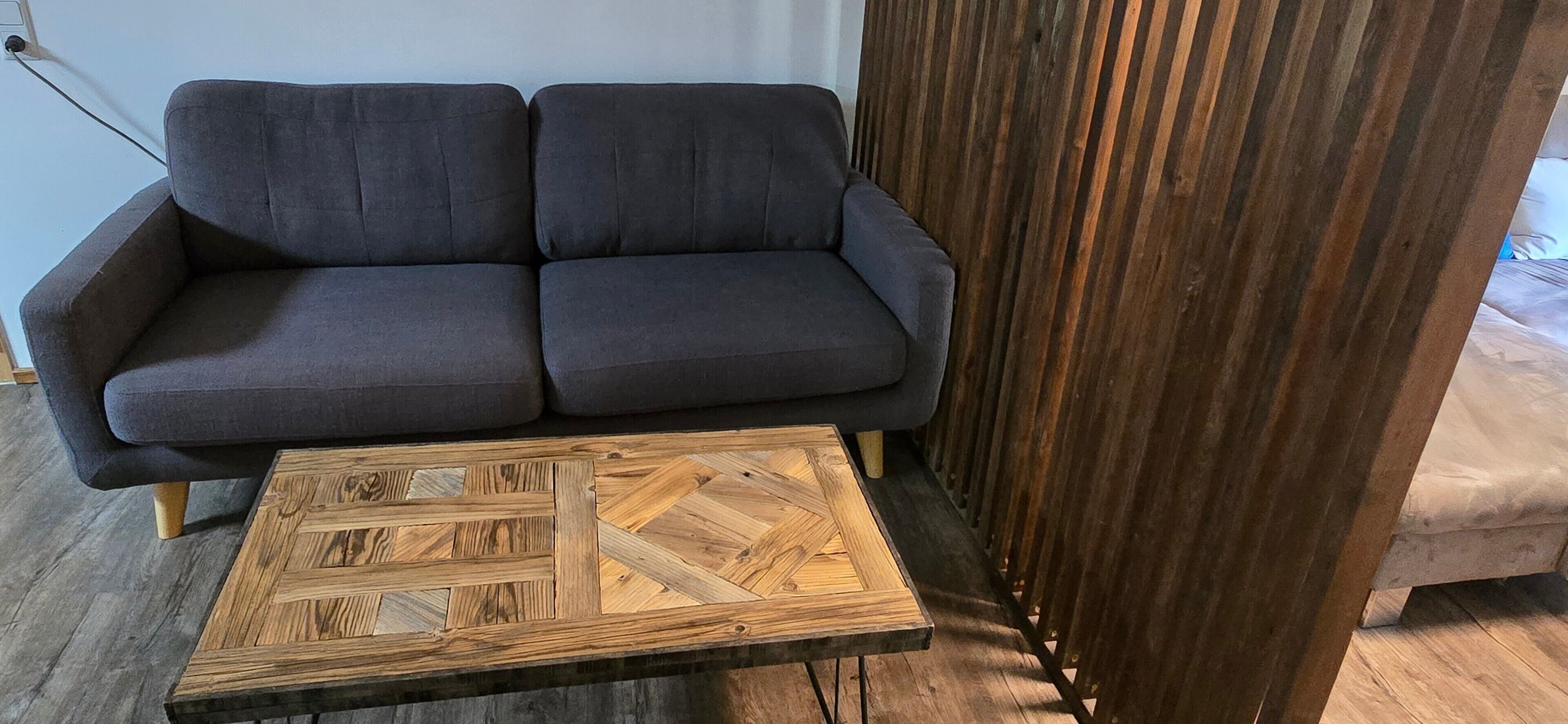 Un sofá oscuro con una mesa de centro de madera con patrón de espiga.