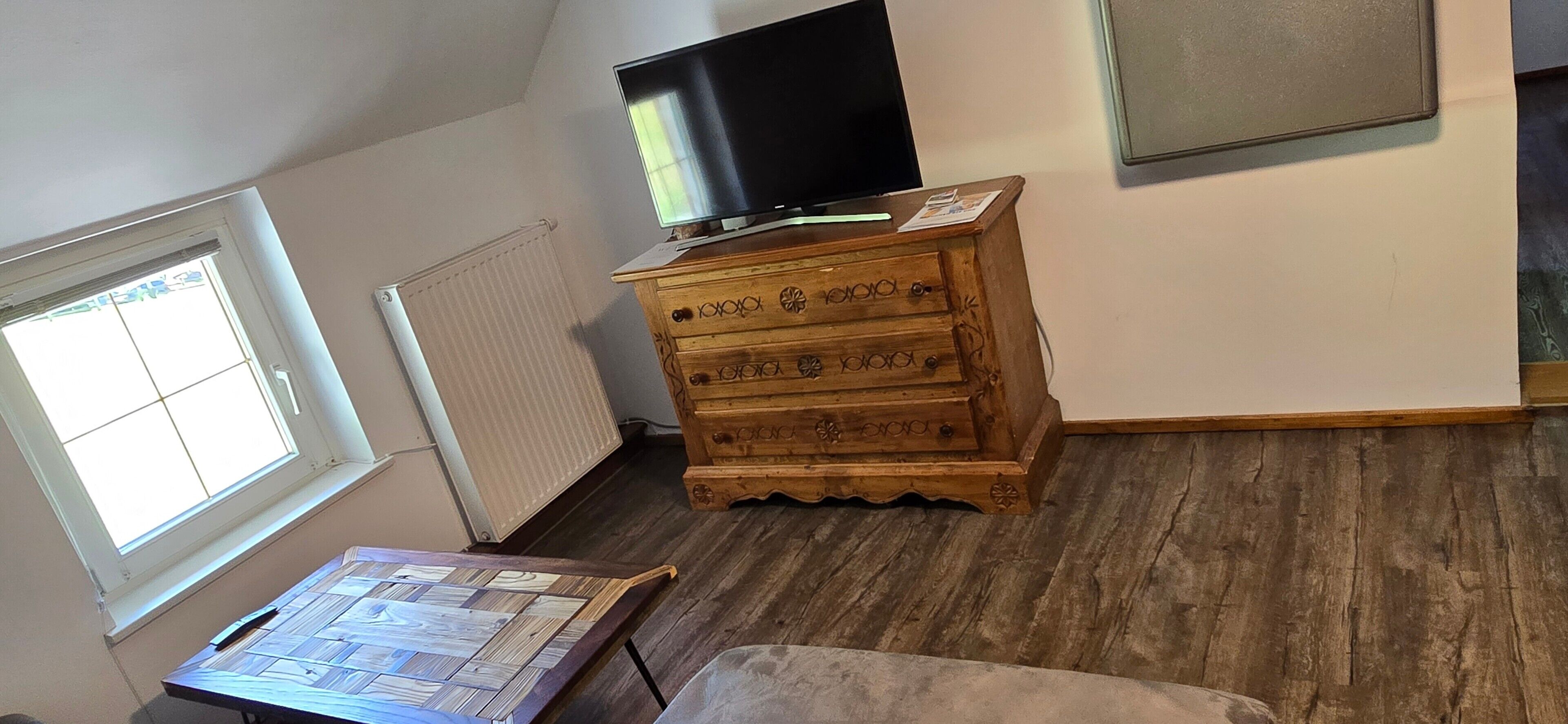 Una habitación con un aparador de madera, un televisor encima y una ventana, además de un radiador.