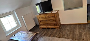 A room with a wooden dresser, a television on top, a window, and a radiator.