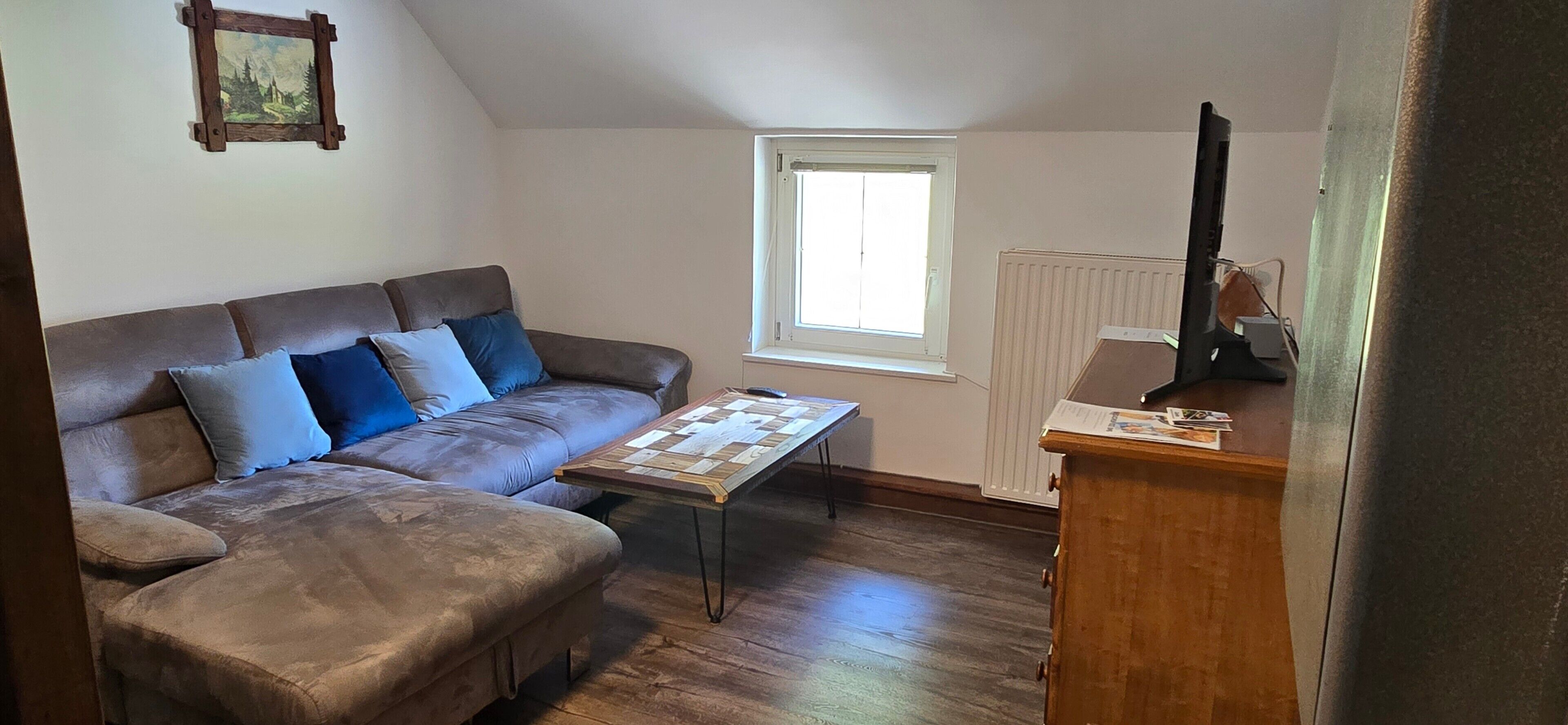 Een gemeubileerde kamer met een bruine bank, een houten salontafel, een radiator en een raam.
