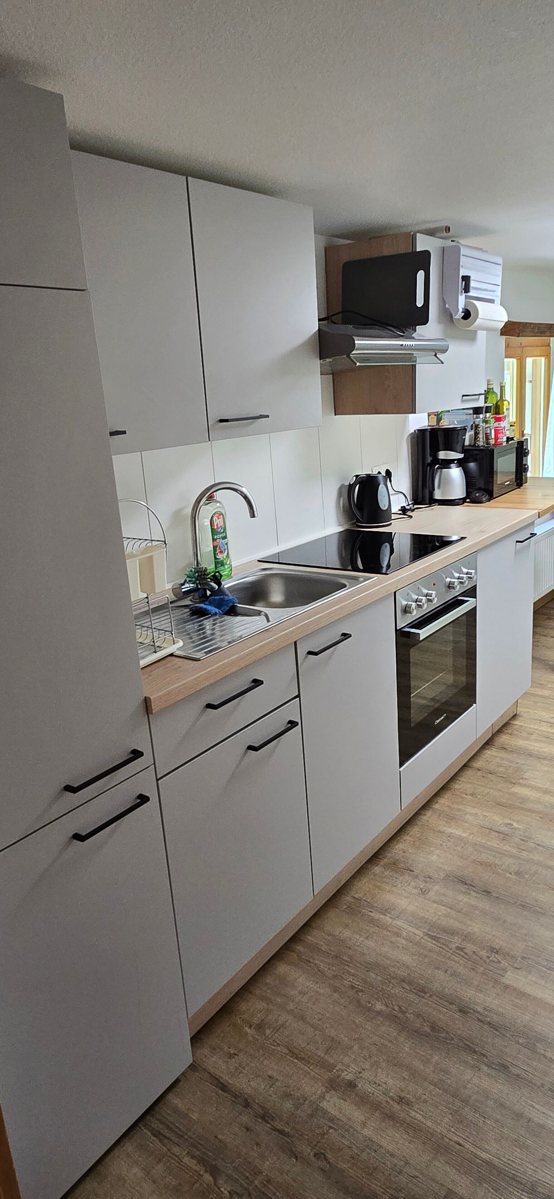 A modern kitchen with white cabinets, a stainless steel sink, a built-in oven, and a microwave above the counter.