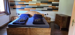 A double bed with a wooden headboard, two bedside tables, and a wall with a wooden plank pattern.