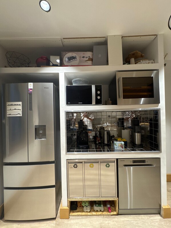 Cocina compacta con refrigerador de acero inoxidable, microondas y lavavajillas.