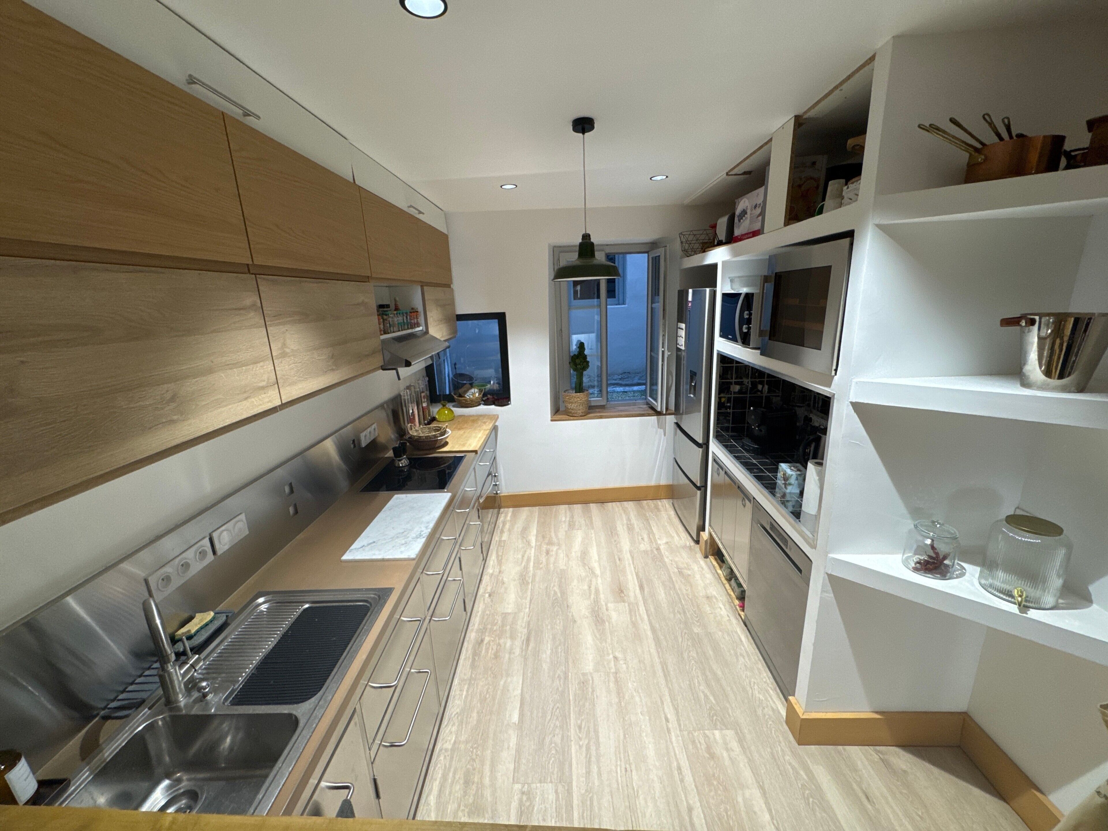 A modern kitchen with stainless steel appliances, wooden cabinets, and a view to the outside.
