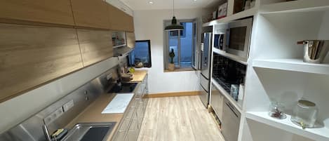 A modern kitchen with stainless steel appliances, wooden cabinets, and a view to the outside.