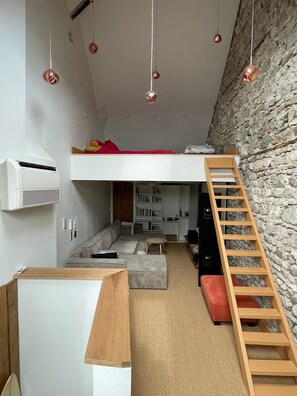 Dormitorio tipo loft con cama litera, pared de piedra, escalera de madera y unidad de aire acondicionado blanca.
