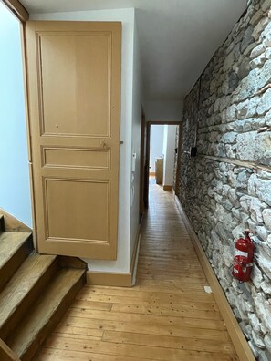 Un pasillo con piso de madera, pared de piedra y un extintor montado en la pared.