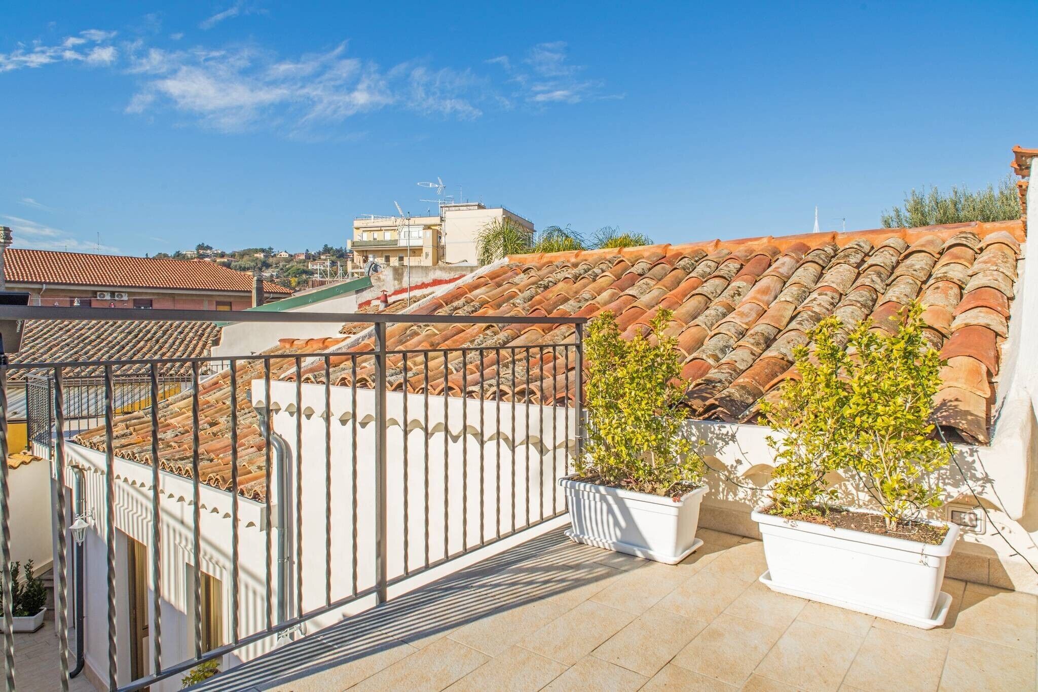 Eine Dachterrasse mit Terrakotta-Fliesen, Blumentöpfen und einem Metallgeländer.