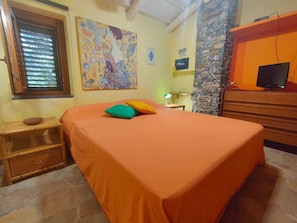 A room with a bed, a nightstand, a desk with a lamp, a stone wall, and a television. - Villa Gioirisia. A retreat for relaxation and nature. X4 (Campania)
