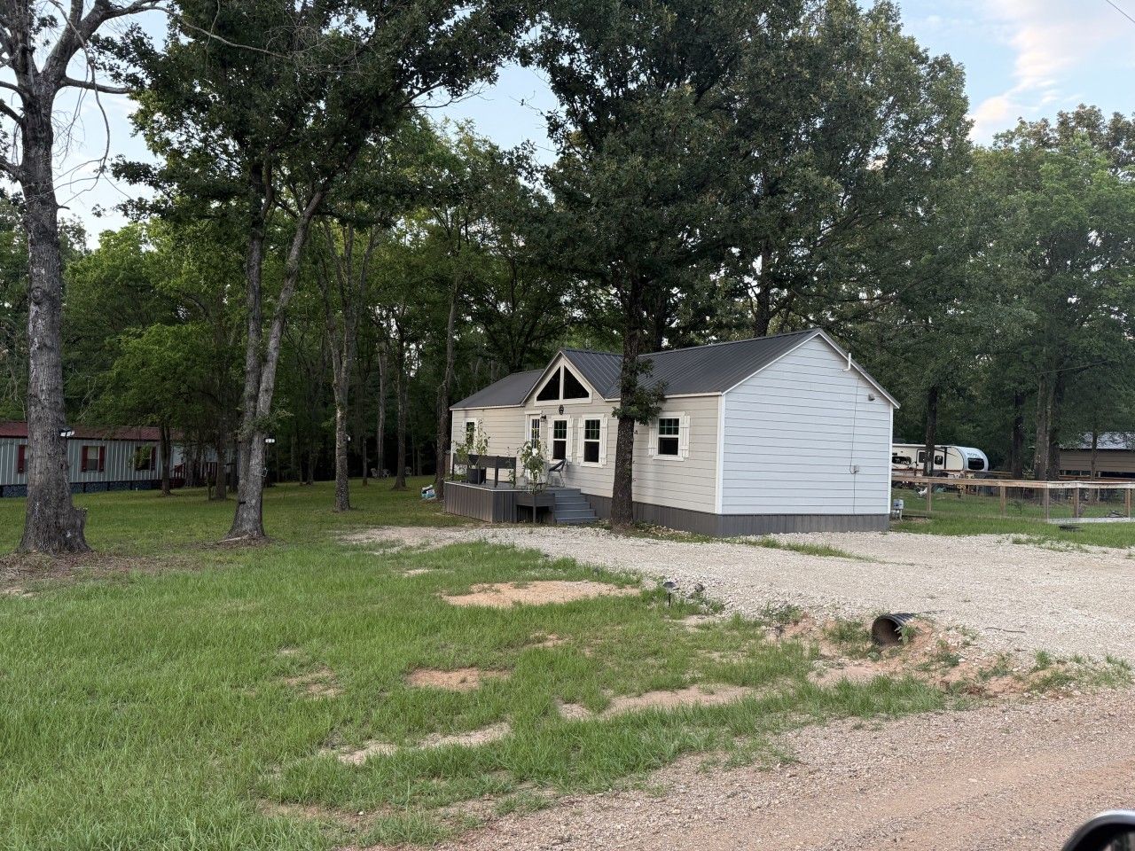A single-story house with a porch, surrounded by trees and a gravel driveway.