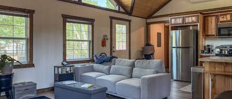 A spacious living room with a sectional sofa, a coffee table, and a dining area with a refrigerator and kitchen counter.