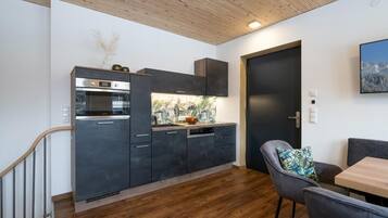 Una cucina moderna con mobili scuri, forno integrato e lavastoviglie. Una scala in legno conduce a un altro livello.