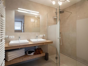 A modern bathroom with two sinks, a glass shower enclosure, and a wooden vanity with towels and a basket.