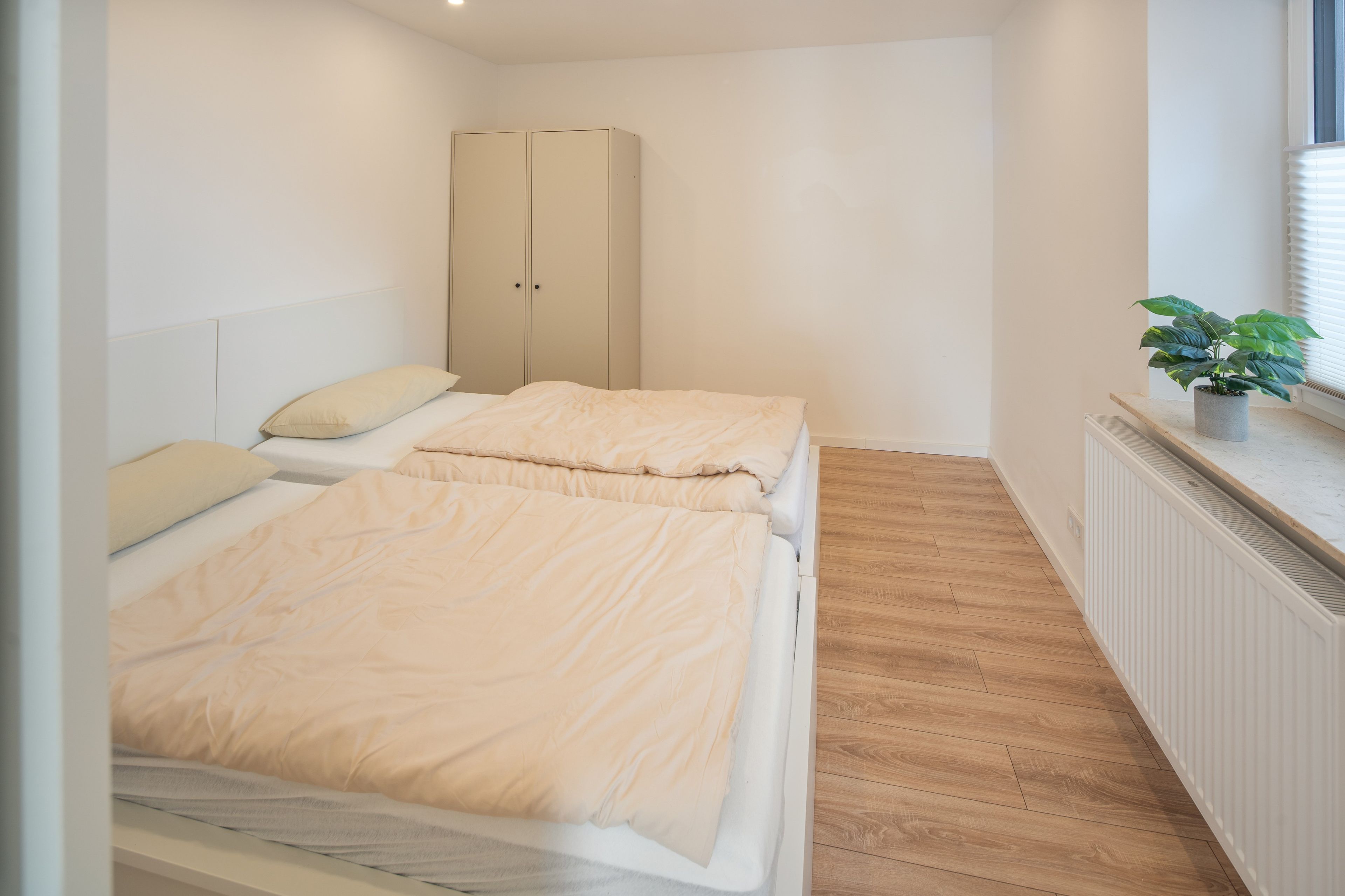 Een slaapkamer met twee bedden, een garderobe, een radiator en een kamerplant.