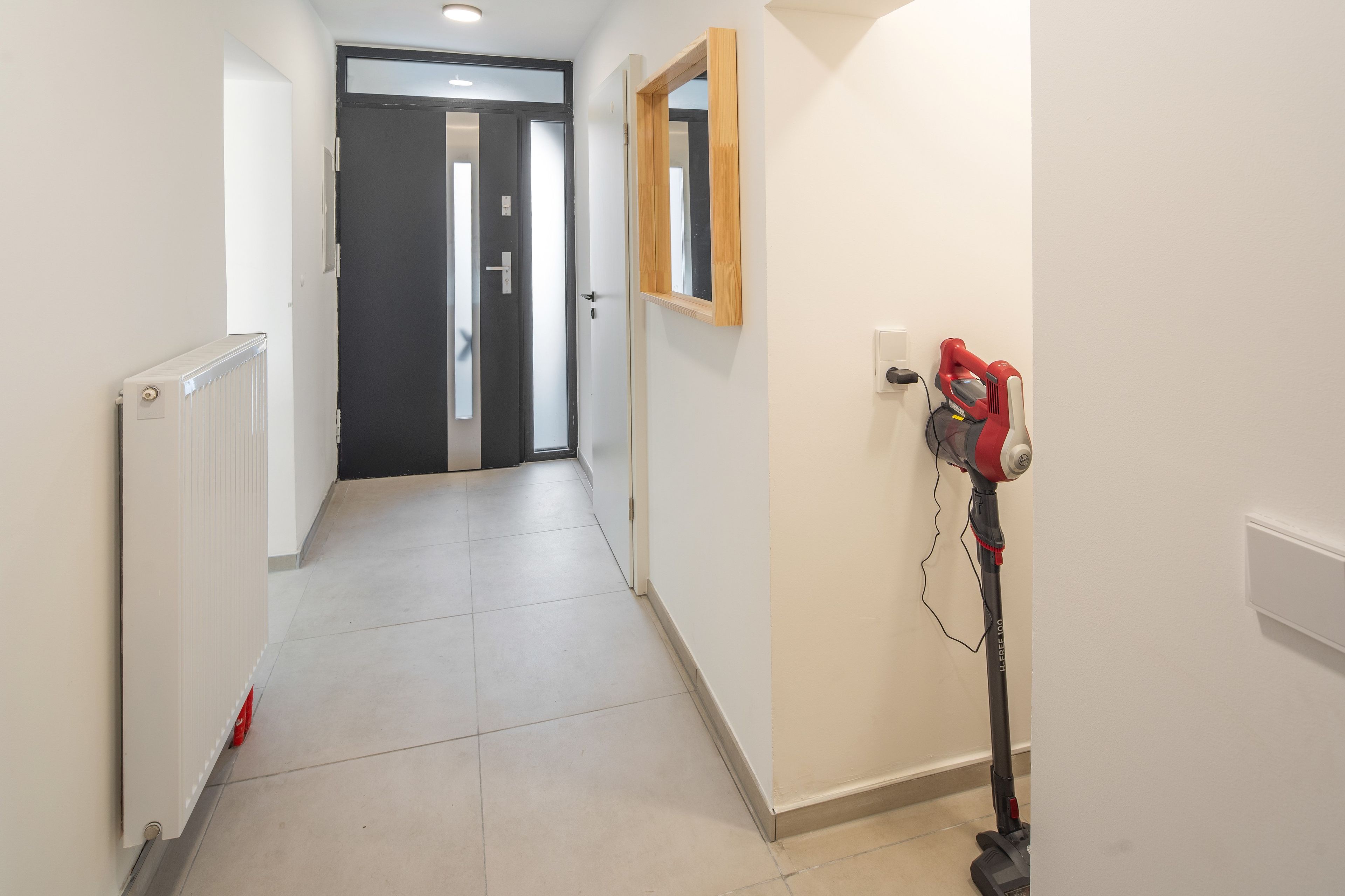 Ein Flur mit Heizkörper, Tür und Staubsauger an der Wand.