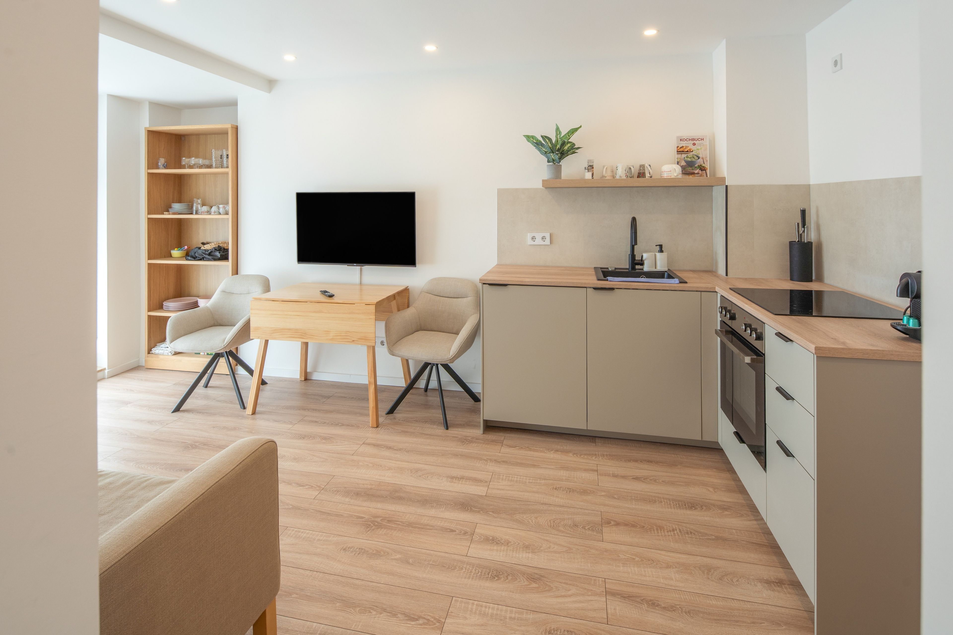 Een moderne keuken met een flatscreen televisie, houten kastjes en een eethoek met twee stoelen.