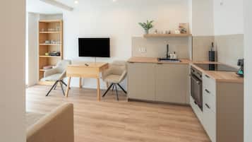 Een moderne keuken met een flatscreen televisie, houten kastjes en een eethoek met twee stoelen.