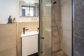 Un bany modern amb dutxa d'ús d'aigua tancada per vidre, un lavabo amb aixeta i un mirall sobre l'altre.