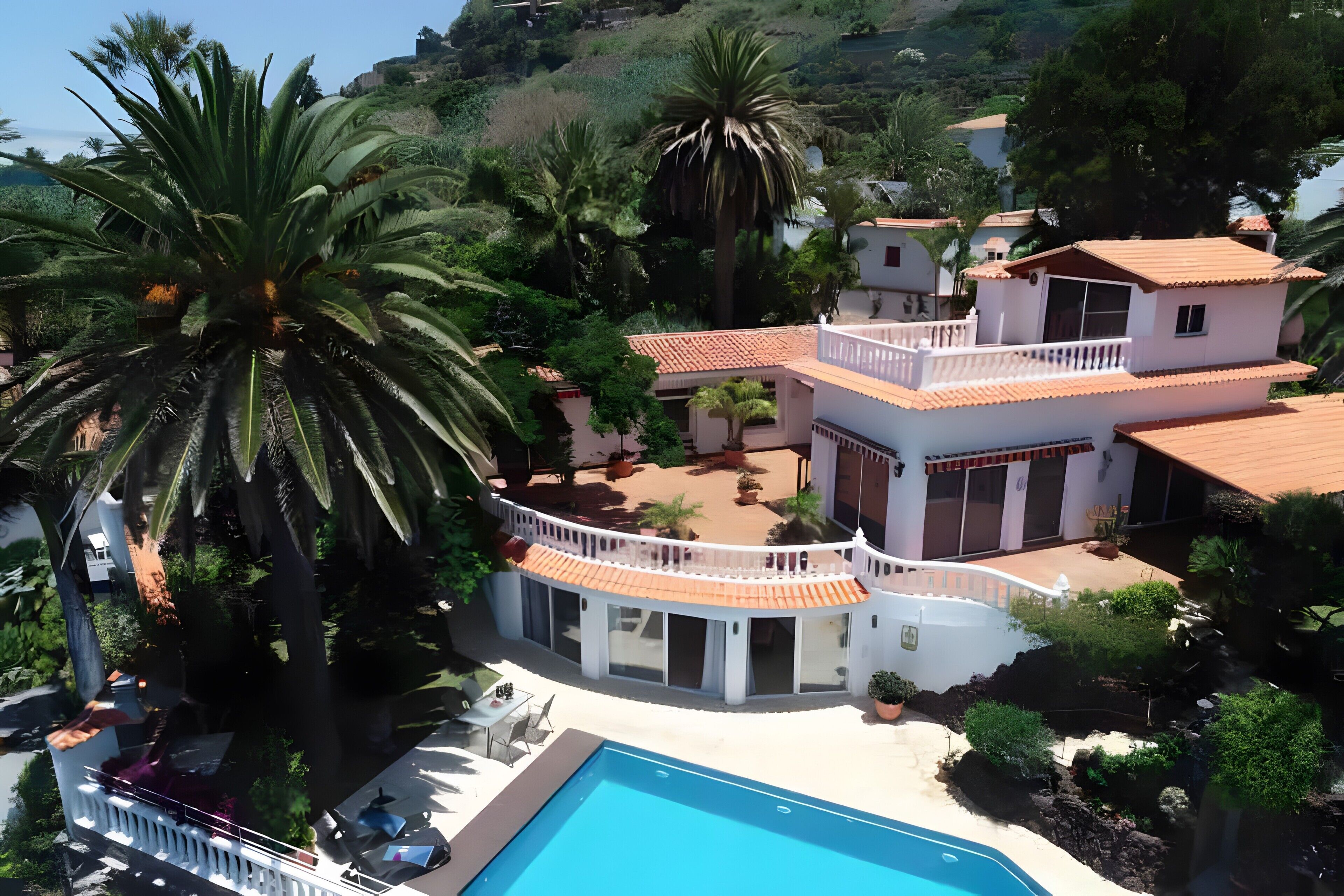 Una casa de dos pisos con piscina, rodeada de palmeras y otra vegetación.