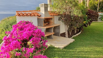 Un patio con una parrilla integrada, rodeado de exuberante vegetación y flores coloridas.