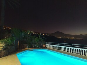 Piscina con vistas a un paisaje urbano y montañas de noche.