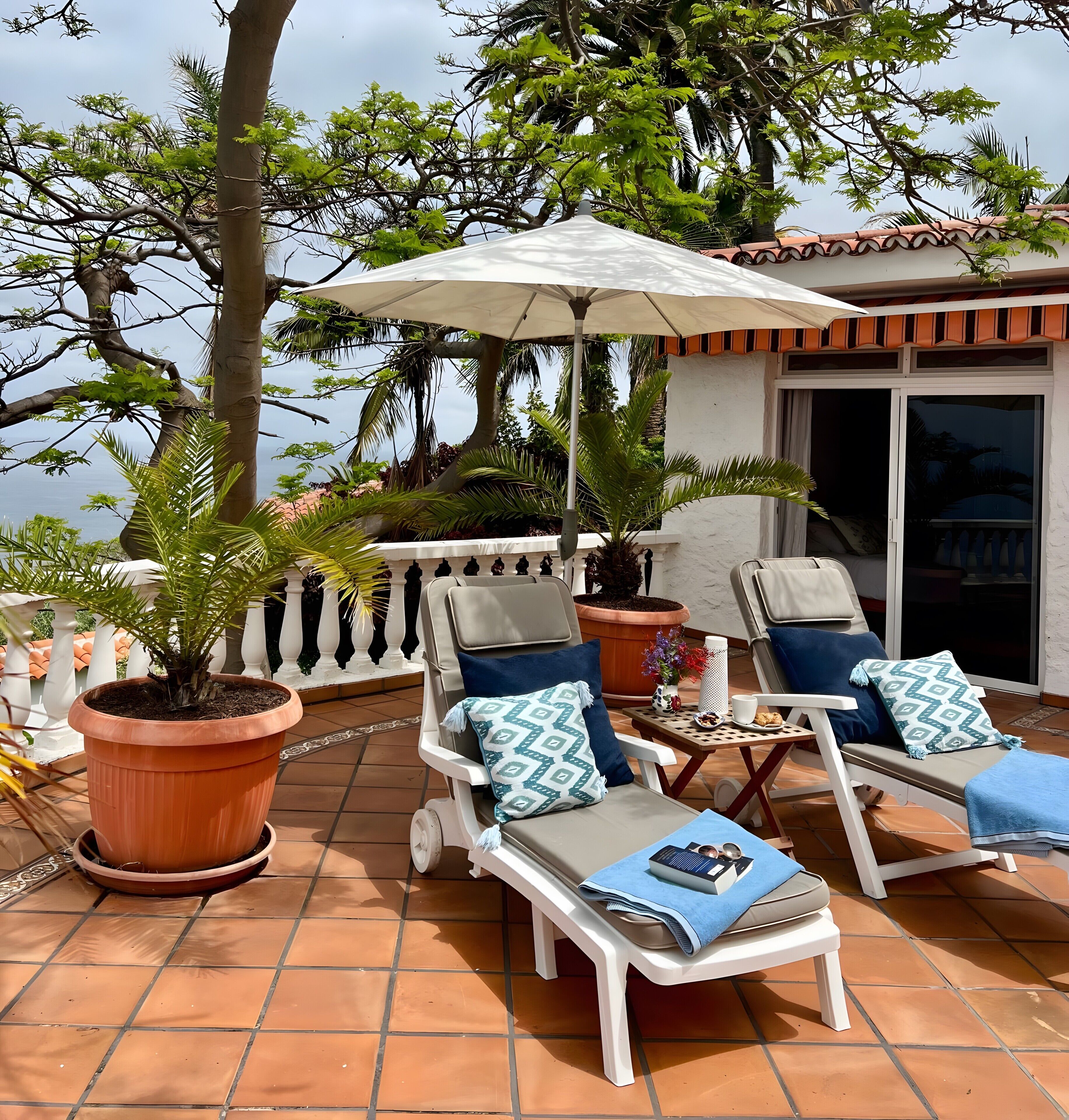 A terrace with two lounge chairs, a table with a cup and a book, and a potted plant.