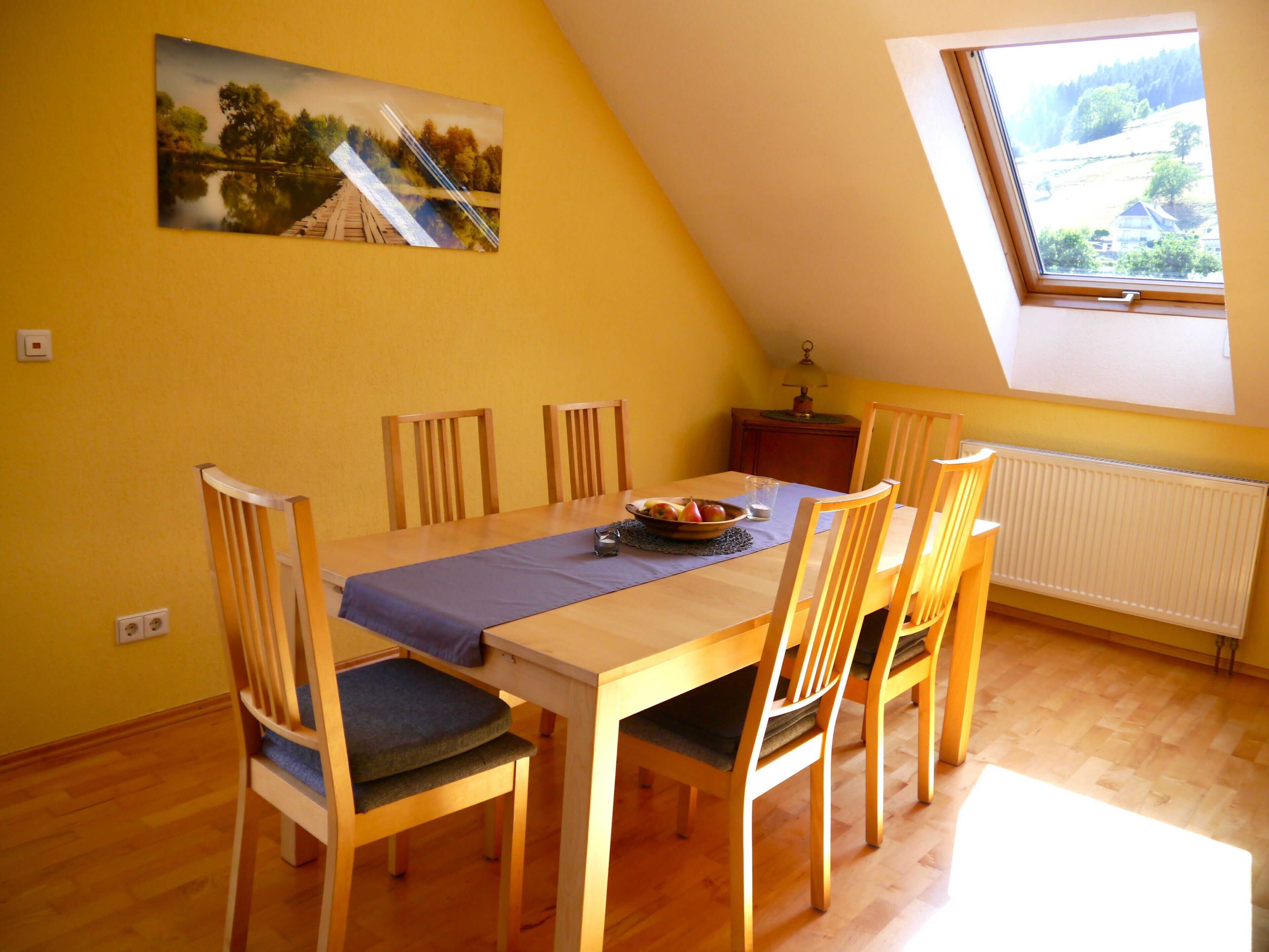 A dining area with a wooden table, chairs, and a painting on the wall.