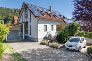 Een modern huis met zonnepanelen op het dak, een garage en een oprit met een geparkeerde auto.