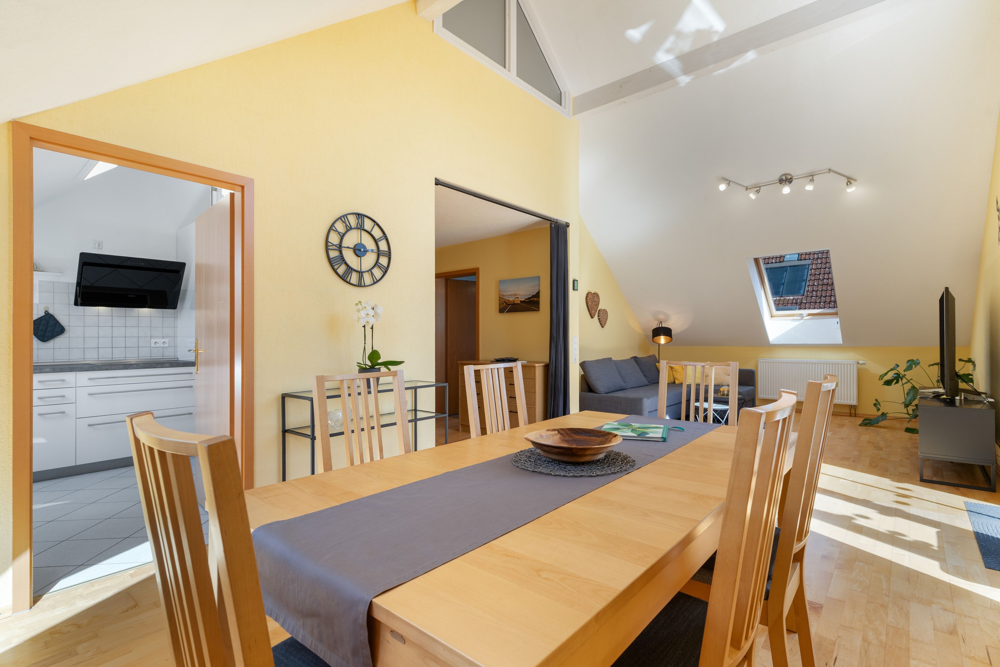 A modern dining area with a wooden table, chairs, and a view into the kitchen.