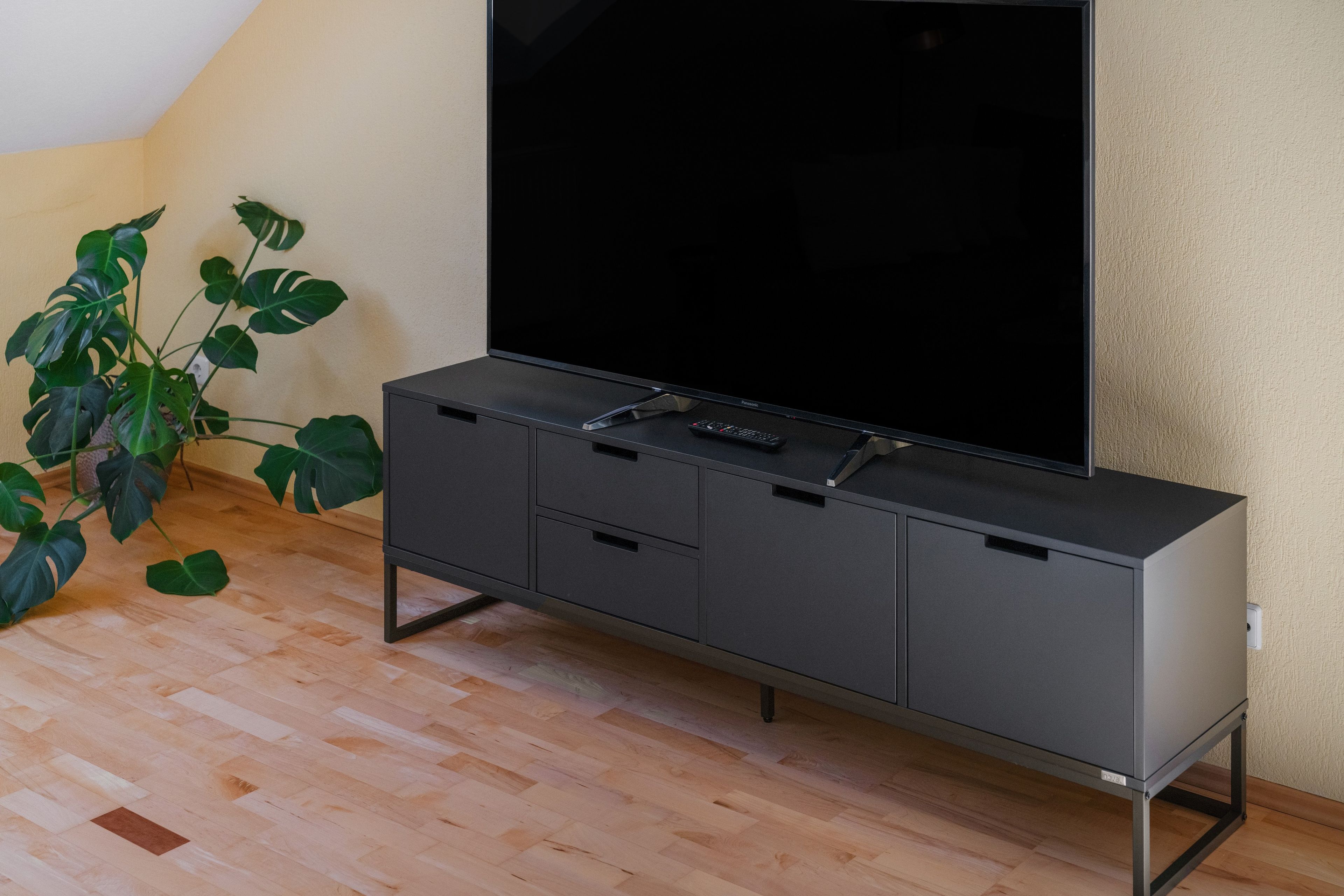 A modern entertainment unit with a flat-screen TV, storage compartments, and a remote control on a wooden floor.