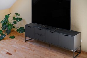 Een moderne tv-meubel met een flatscreen televisie, opbergruimte en een afstandsbediening op een houten vloer.