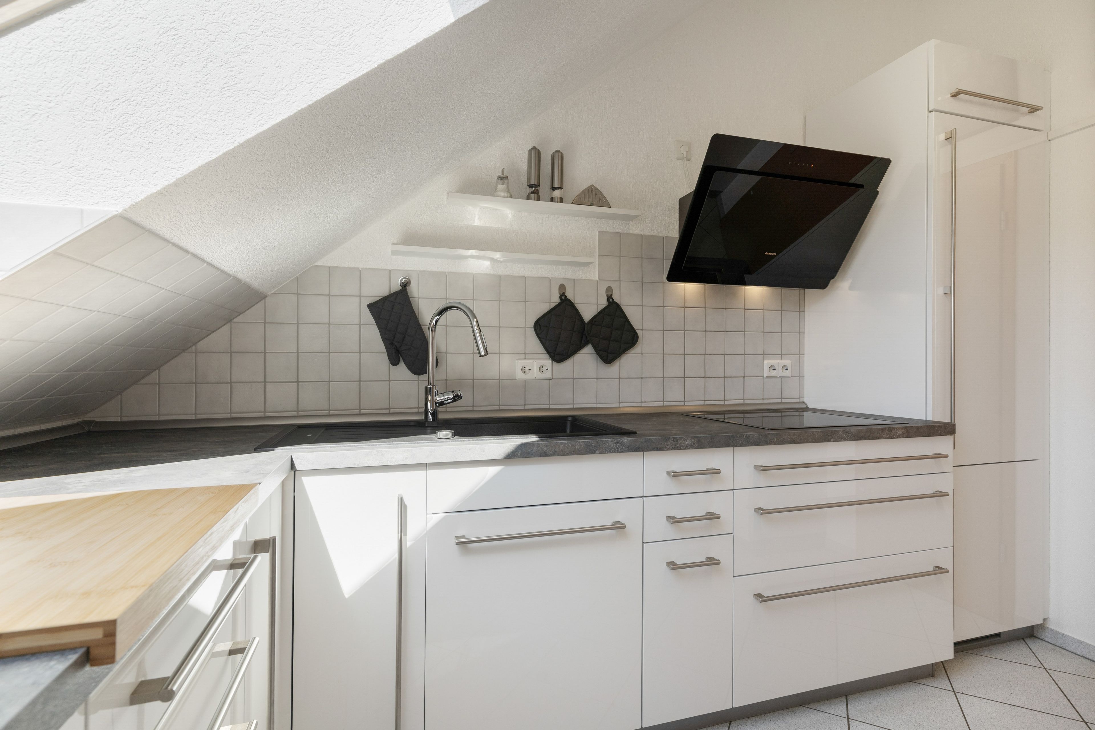 Una cocina moderna con armarios blancos, una estufa negra y un protector contra salpicaduras de azulejos.