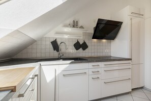 A modern kitchen with white cabinetry, a black stove, and a tiled backsplash. - Apartment 'Haus Schlössleblick' with Mountain View, Balcony and Wi-Fi (Oberwolfach)