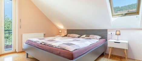 A bedroom with a bed, a bedside table, a lamp, and a window.