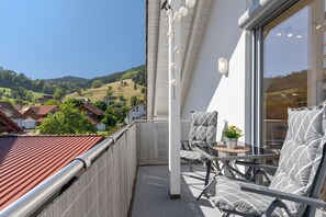 A balcony with a view of a hilly landscape, a table with chairs, and a potted plant. - Apartment 'Haus Schlössleblick' with Mountain View, Balcony and Wi-Fi (Oberwolfach)