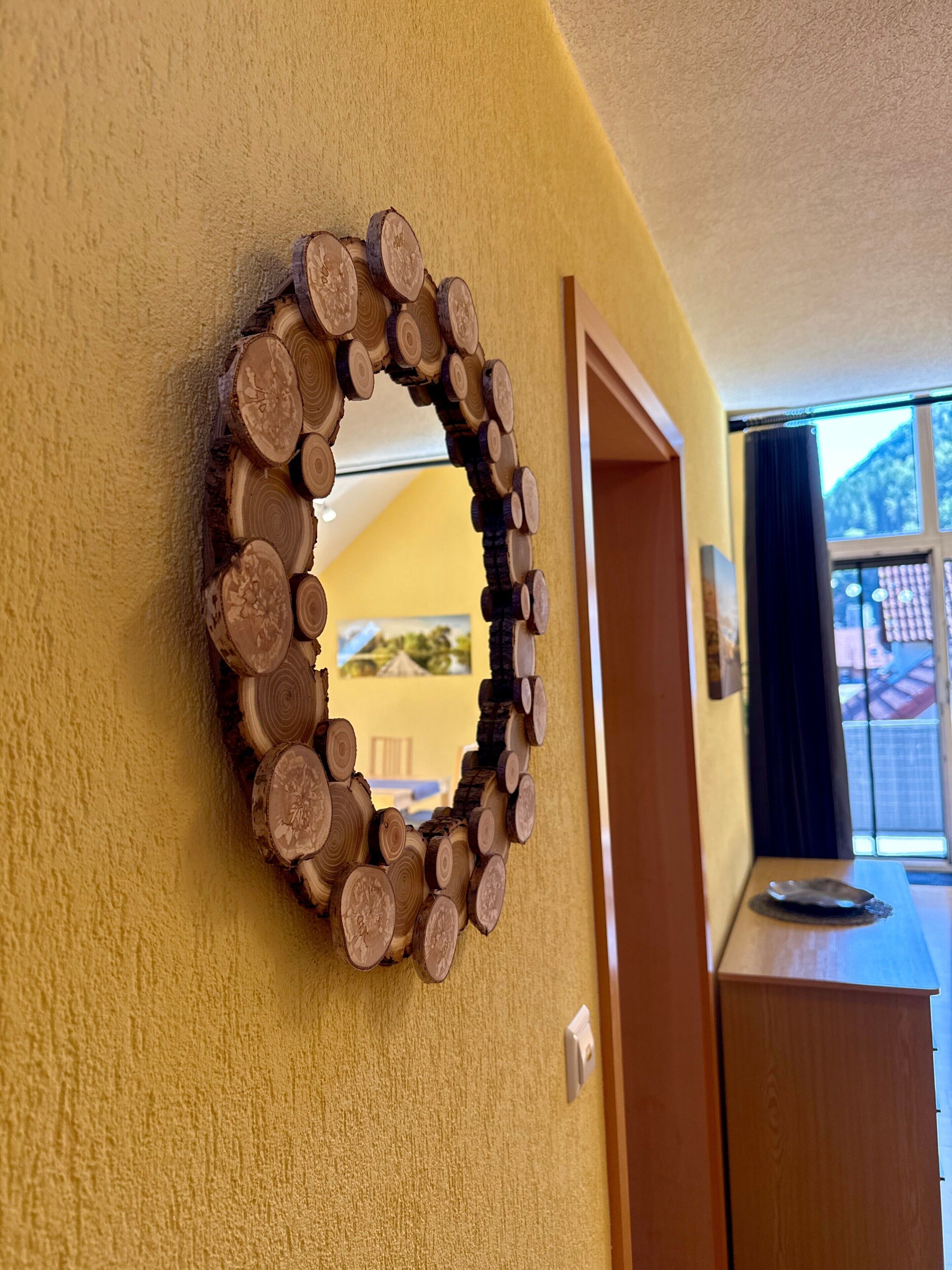 A circular mirror with a wooden frame on a yellow wall.