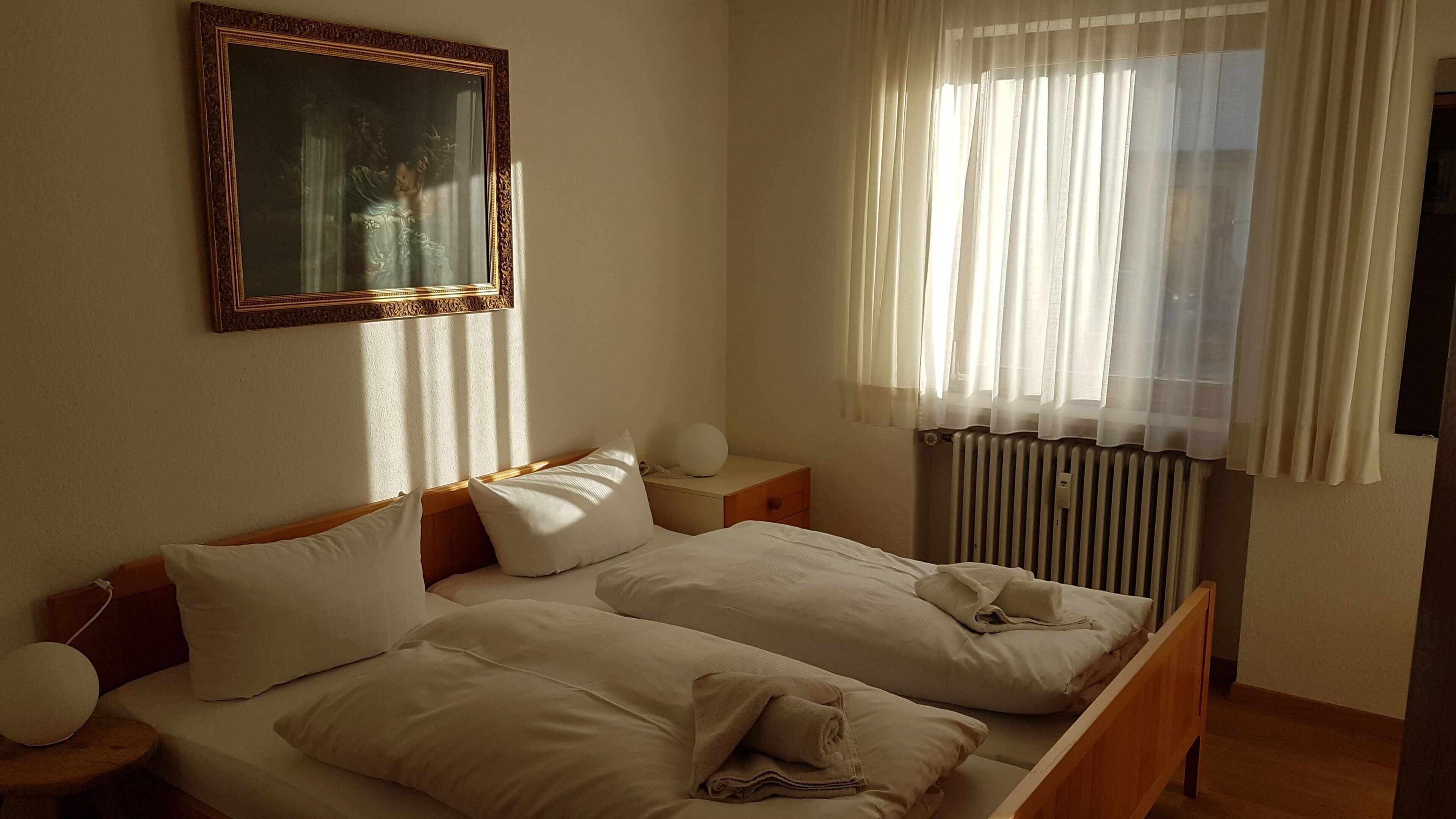 En dobbeltseng med hvide sengetøj, et natbord med lampe og en radiator.