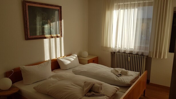 Una cama doble con sábanas blancas, una mesita de noche con lámpara y un radiador.