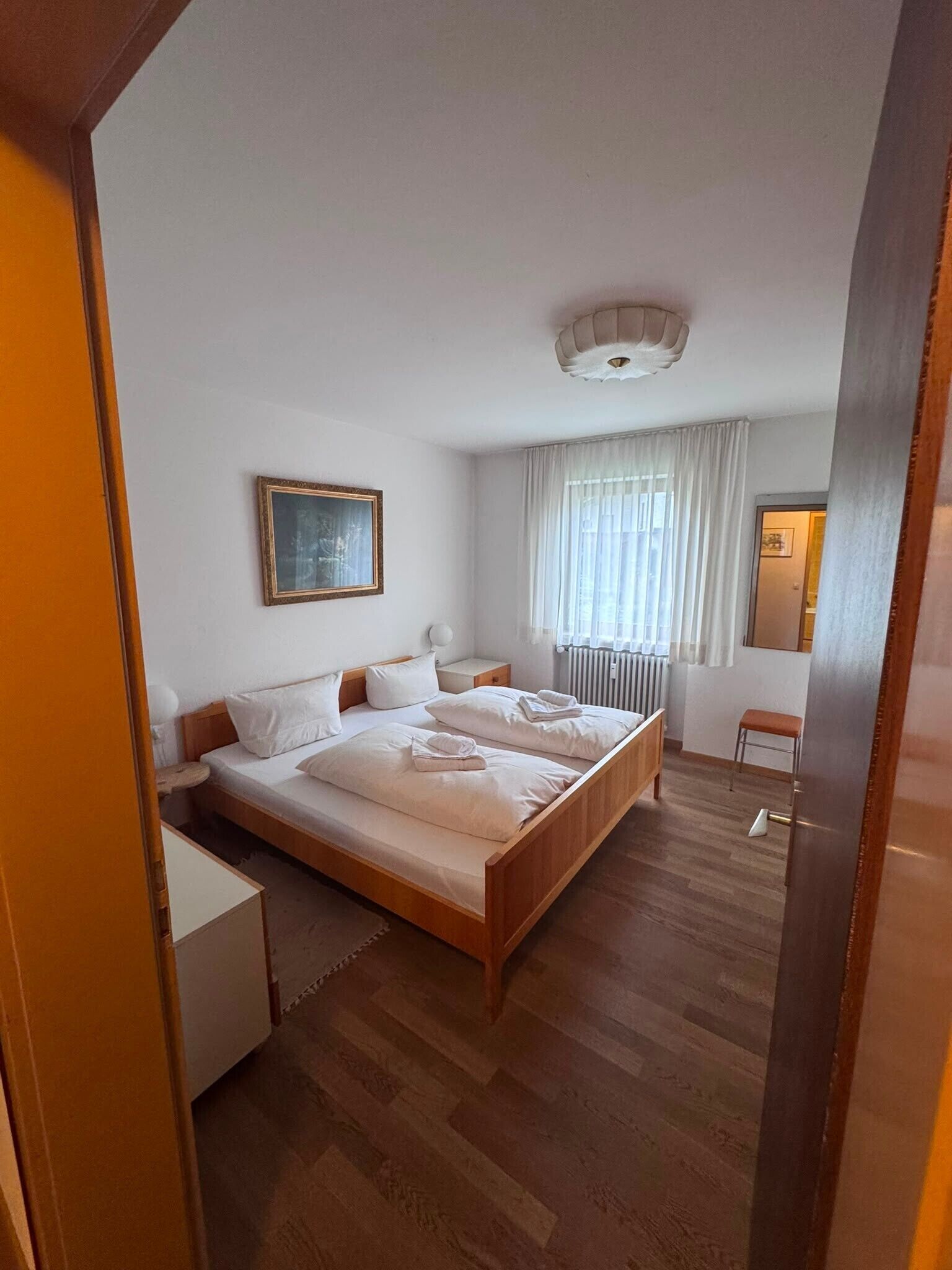 Habitación de hotel con una cama grande, una mesita de noche, una silla, una ventana con cortinas y un aplique de techo.