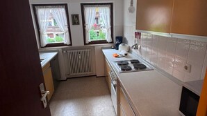 Una cocina compacta con estufa integrada, un radiador y dos ventanas con cortinas.