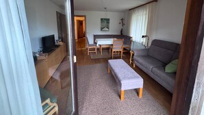 Una sala de estar con sofá, televisor, mesa de comedor con sillas y un cuadro en la pared.