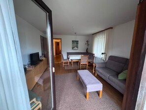 A living room with a sofa, a TV, a dining table with chairs, and a painting on the wall.