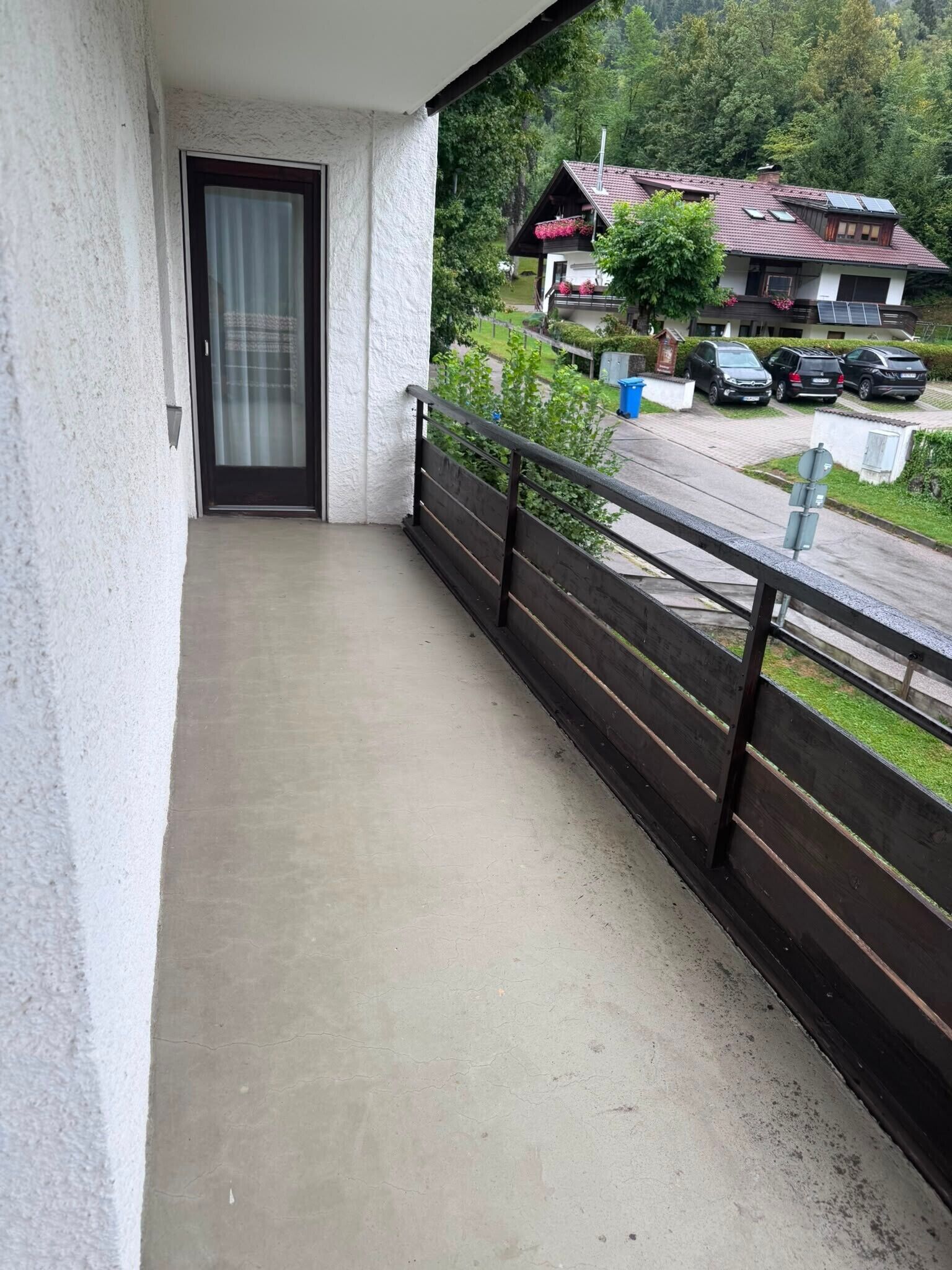 Ein Balkon mit Betonboden, Holzgeländer und einer Tür zu einem Innenraum.