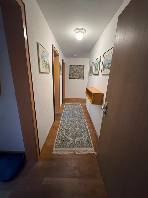 A hallway with wooden flooring, a patterned rug, and framed artwork on the walls.