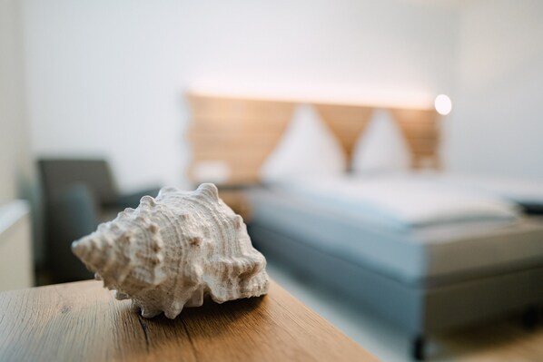 A wooden table with a seashell in the foreground and a blurred hotel room in the background.