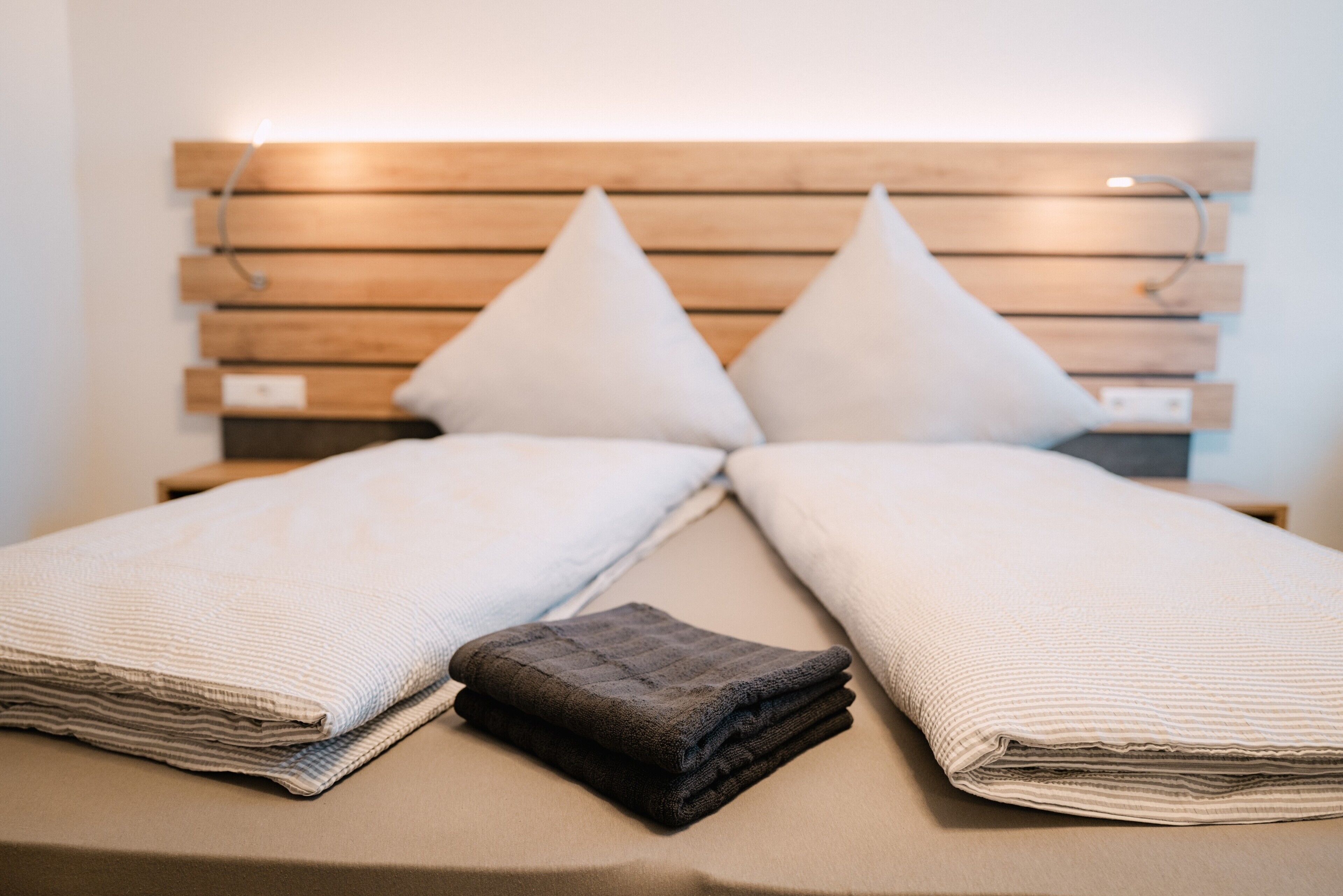A neatly made bed with a wooden headboard, two pillows, and folded blankets.