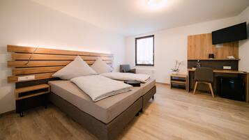 Ein modernes Schlafzimmer mit einem hölzernen Kopfteil, einem Bett mit Kissen, einem Nachttisch, einem Schreibtisch mit Stuhl, einem Fernseher und einem Fenster.